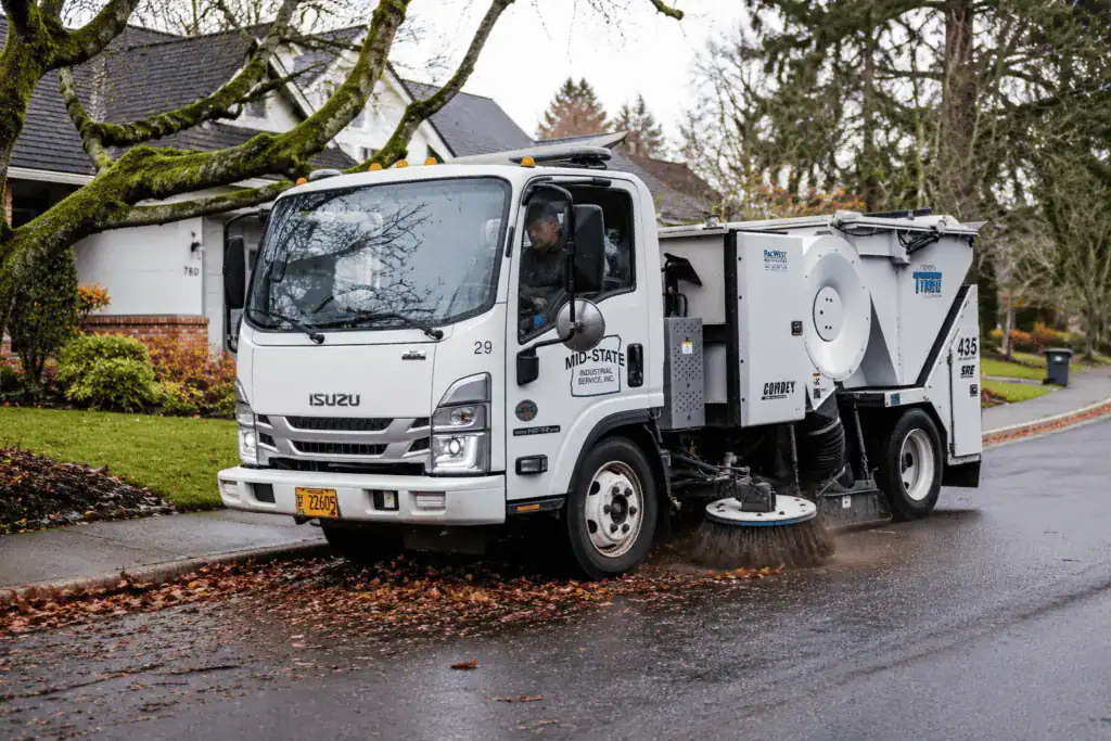 Mid-State TYMCO street sweeper cleaning a tree-lined residential road.